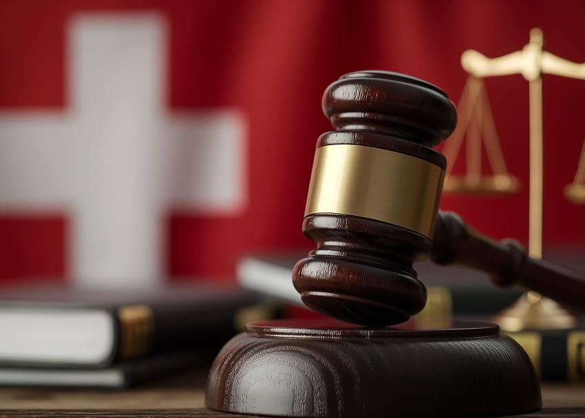 Gros plan sur un marteau de juge en bois sombre à anneau doré, accompagné d'une balance de la justice et de livres de droit, sur fond de drapeau suisse — illustration du cadre légal et fiscal helvétique.